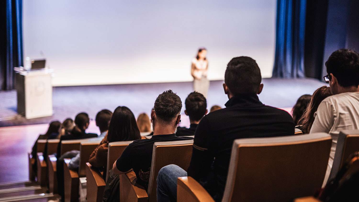 Female speaker giving a talk to an audience in a conference hall.